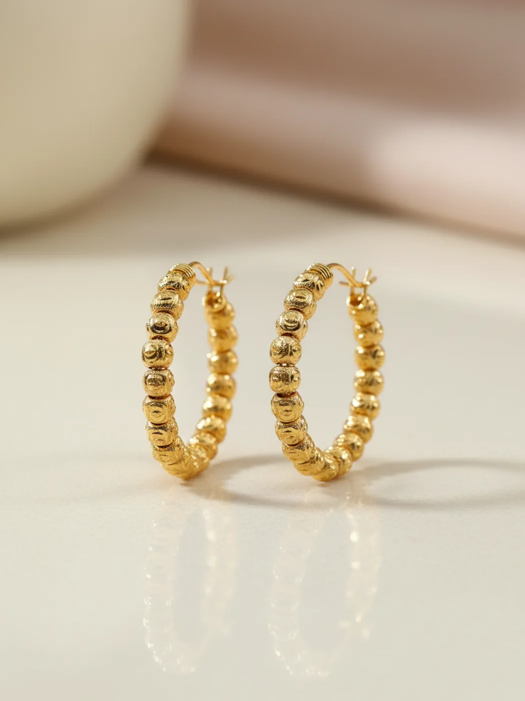 Gold-plated beaded hoop earrings on a cream background