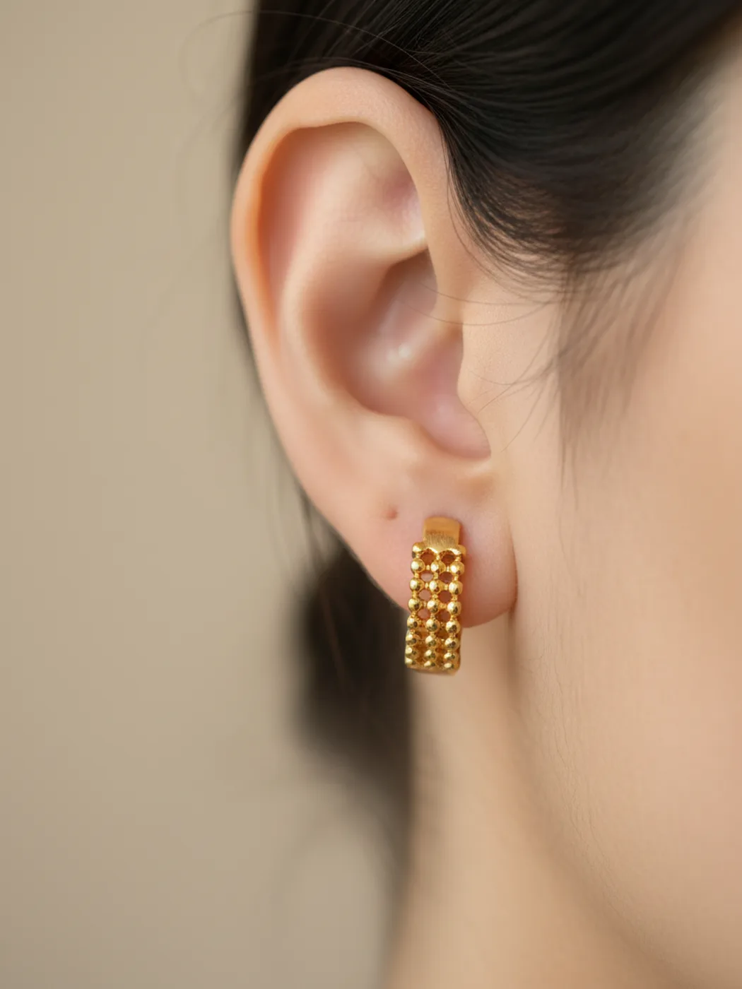 Gold-plated beaded huggie hoop earrings worn on a model’s ear