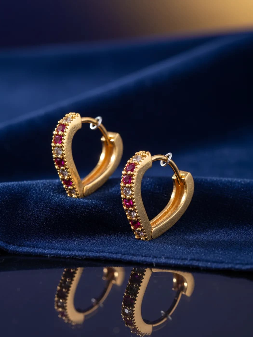 Heart-shaped gold hoop earrings set with red and white stones on blue velvet