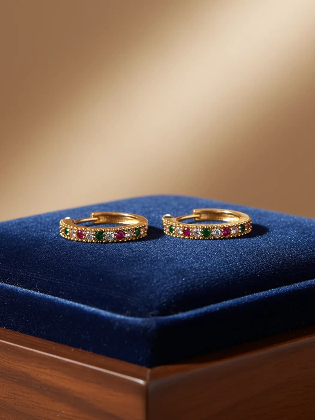Gold huggie hoop earrings set with multicoloured stones on blue velvet